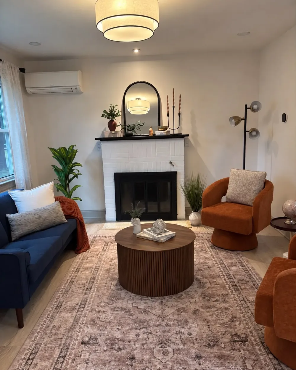 After: living room with a fluted round coffee table, rust swivel chairs, and a styled mantel