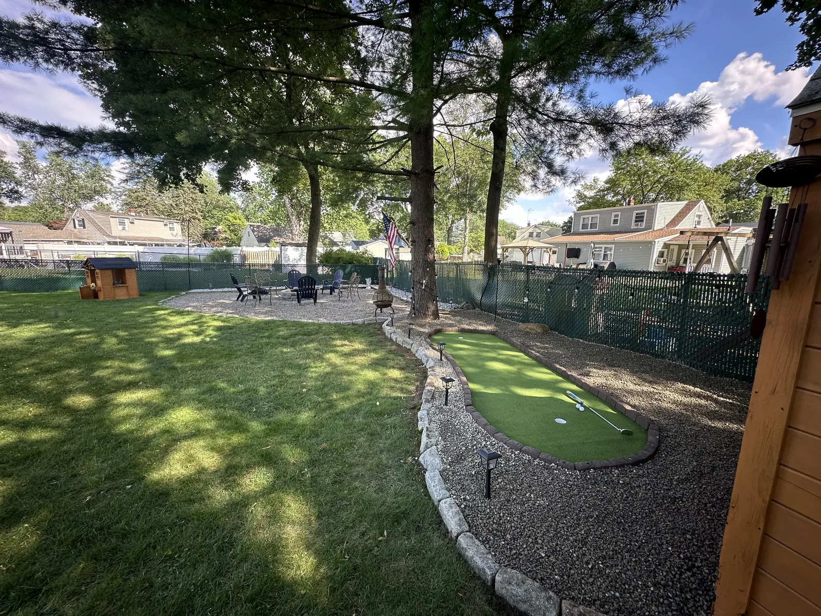 Backyard with a putting green edged in paver stone, gravel bed, lawn, and a fire pit seating area