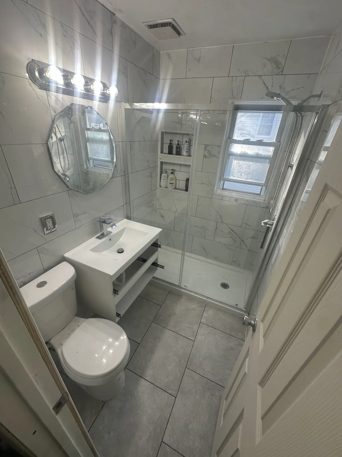 Renovated bathroom with large format marble look tile, glass shower, recessed niche, and floating vanity