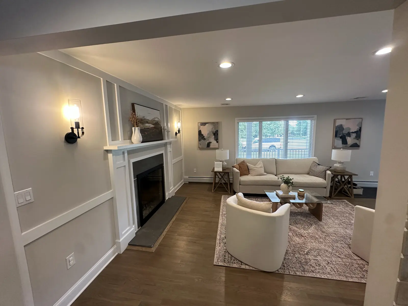 Living room with a custom white fireplace surround, wall paneling, sconces, and refinished hardwood floors