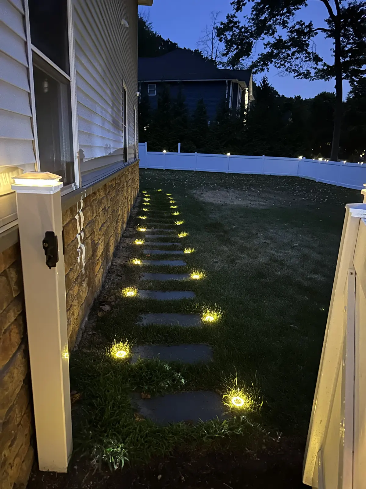 Stone walkway lit at dusk by in-ground landscape lights along the side of a home