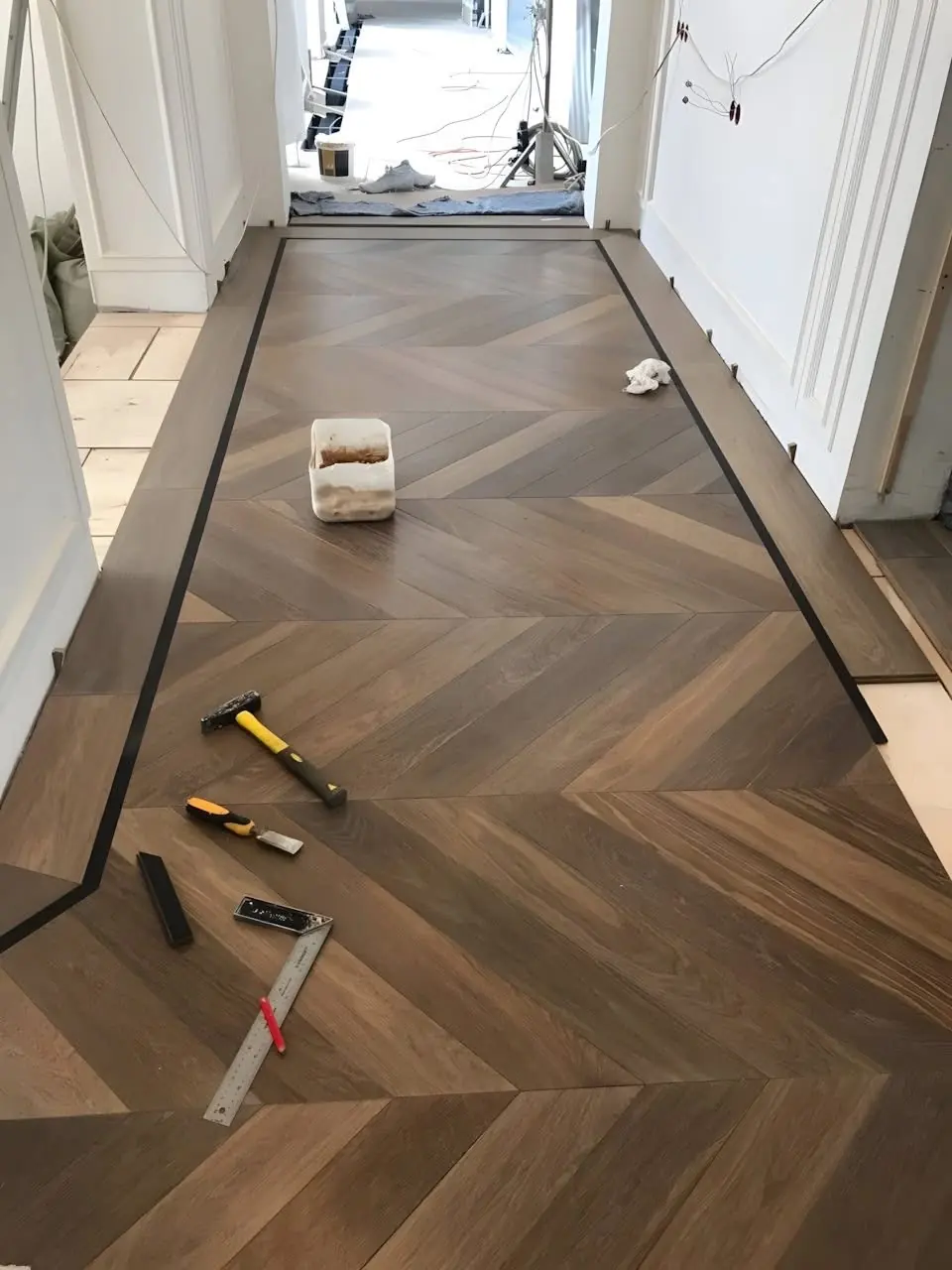 Chevron pattern hardwood floor being installed with a dark inlaid border