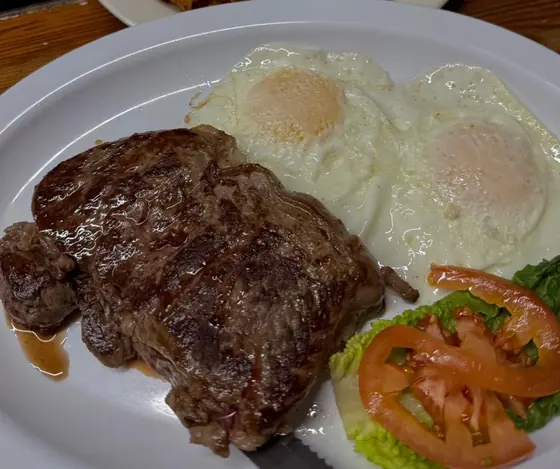 Steak with two eggs over easy and sliced tomato